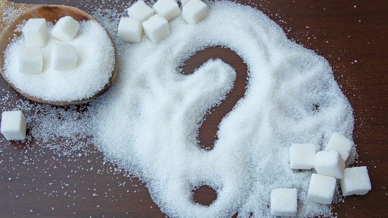 Sugar cubes and sugar on a table with a question mark drawn in the sugar