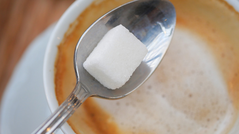 Spoon holding a cube of sugar over a cup of coffee