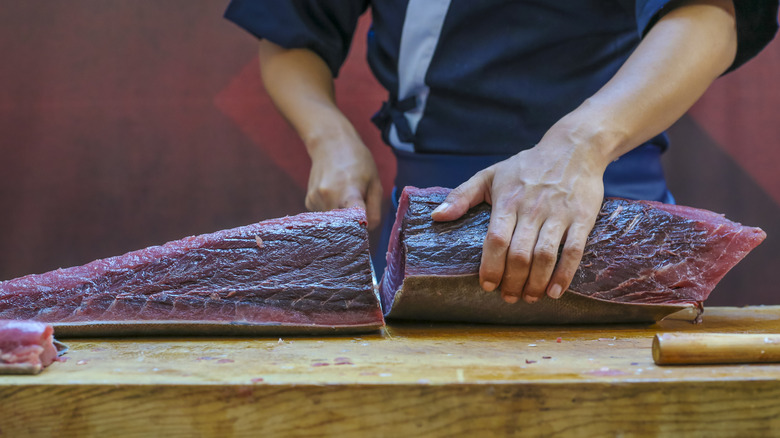 a large side of deep red tuna sliced in half by a sushi chef