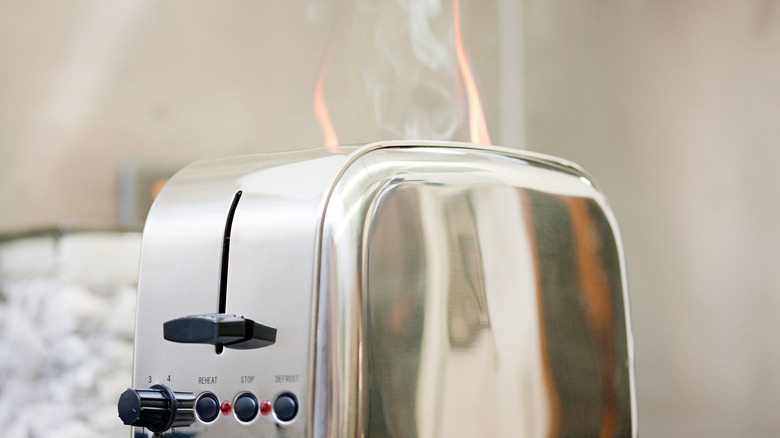Stainless steel toaster with a faint flame and smoke coming out of it