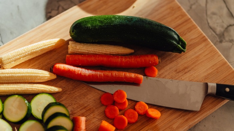 a chef's knife with carrots, zucchini and corn on a wooden cutting board