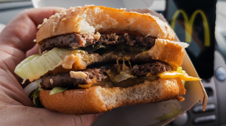 A person holding a McDonald's Big Mac burger that has a bite taken out of it so you can see the layers of ingredients