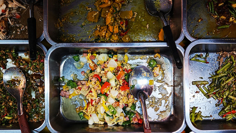 Half-empty metal containers of vegetables and stir-fry with serving spoons