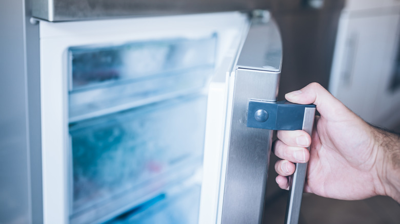 A hand opens a home freezer, revealing its clouded drawers within