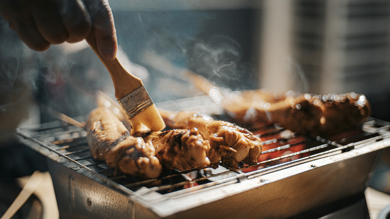 A hand brushing barbecue meat on a tiny grill