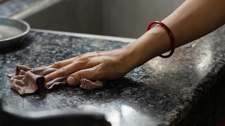 Hand cleaning a black granite countertop with a rag
