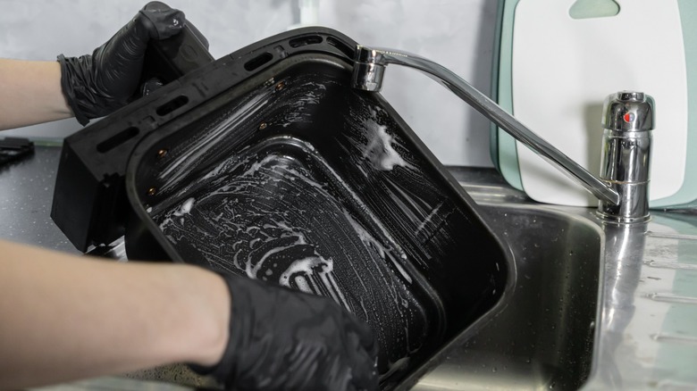Someone with black gloves washing an air fryer basket in sink