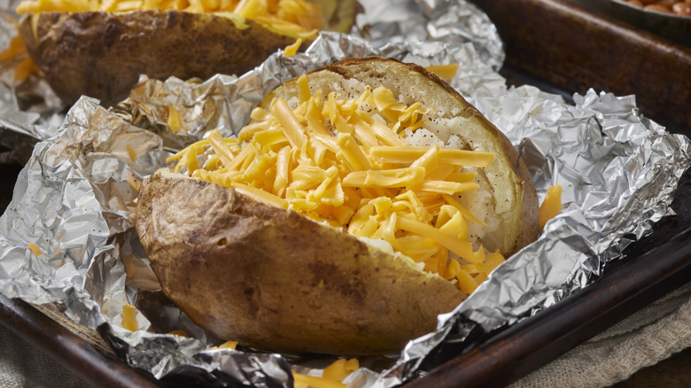 A baked potato topped with cheese on foil