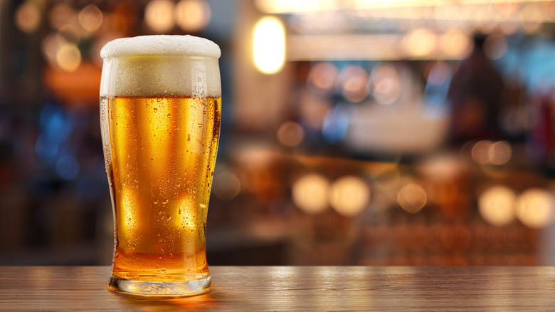 a chilled pint glass of beer sits on a wooden table