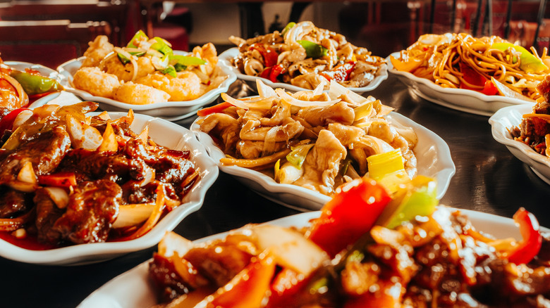 Various stir fry dishes in white plates on black table, including noodles, chicken, and shrimp