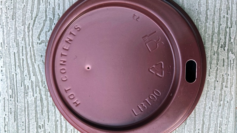 A brown plastic coffee cup lid showing the drinking hole and the tiny vent hole