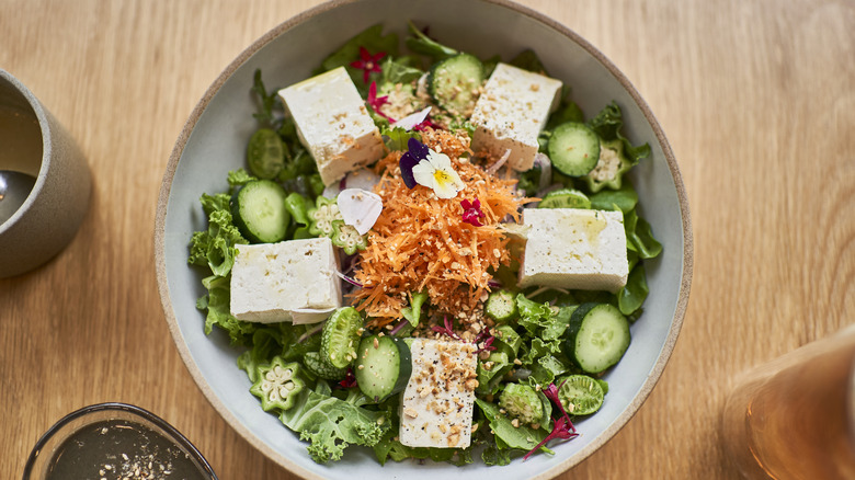 aerial shot of salad with carrots, cucumber and okra topped with tofu in a gray bowl