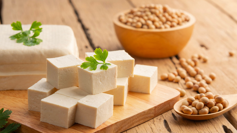 cubed tofu on a wooden cutting board with soybeans in background