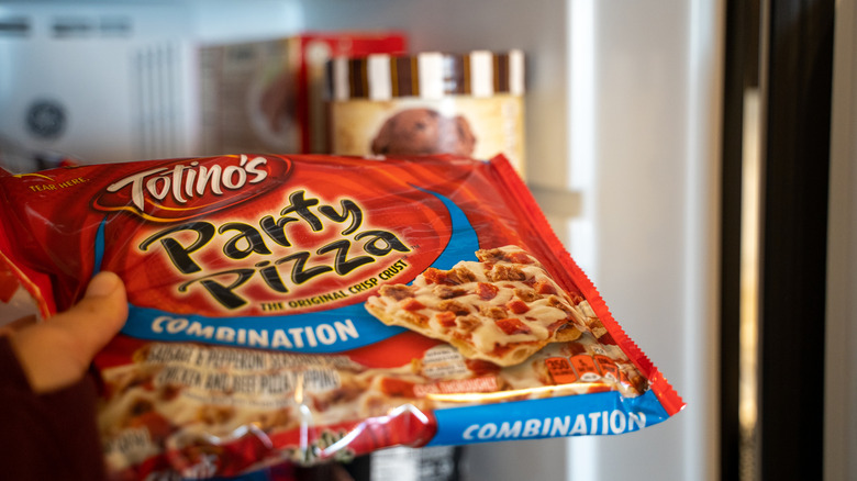 Hand pulls out a Totinos Party Pizza frozen pizza out of freezer