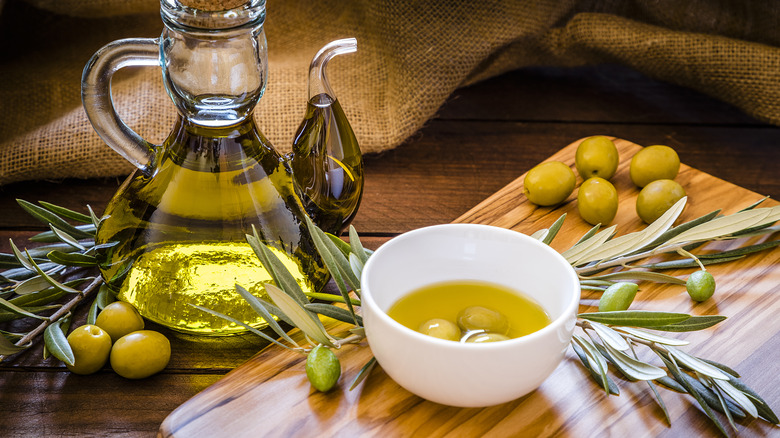 olives and olive leaves beside glass bottle of olive oil and bowl of olives in olive oil