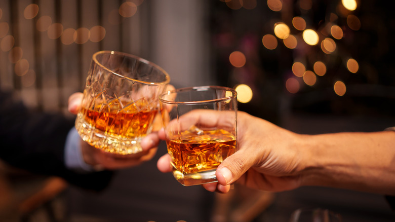 Two people, only their arms and hands and view, clinking glasses of whisky in a cheers gesture