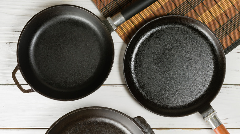 Three cast iron pans on white wooden table