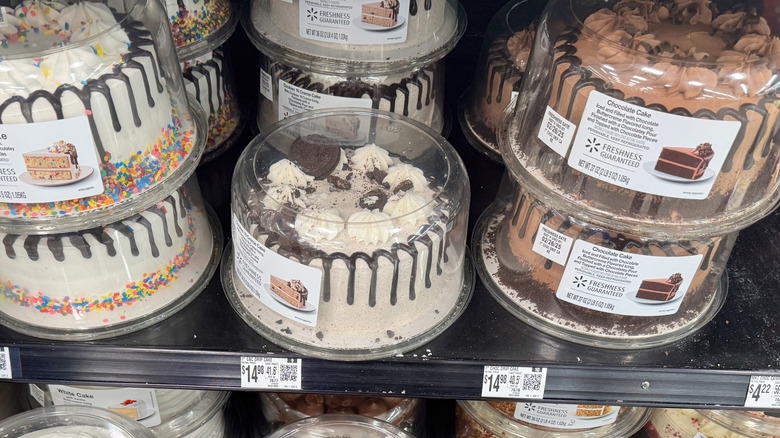 A selection of cakes on a Walmart shelf including the confetti cake, cookies and cream cake, and a chocolate cake stacked together