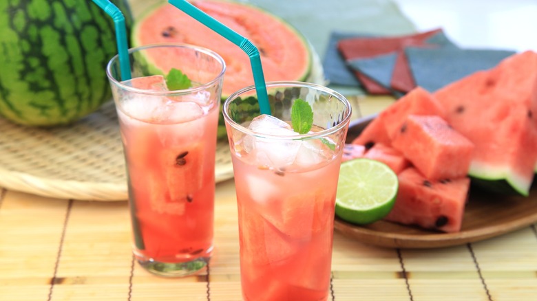 Two glasses of watermelon juice with cut up watermelon behind them