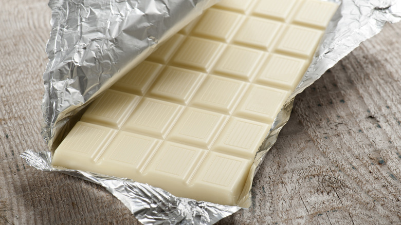 White chocolate bar in aluminum foil on a wooden surface