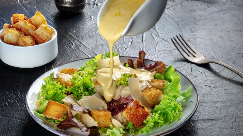 Dressing being poured onto Caesar salad