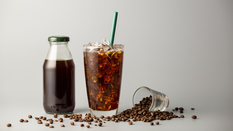 Iced americano in a glass and bottle, and coffee beans spilling out of a cup