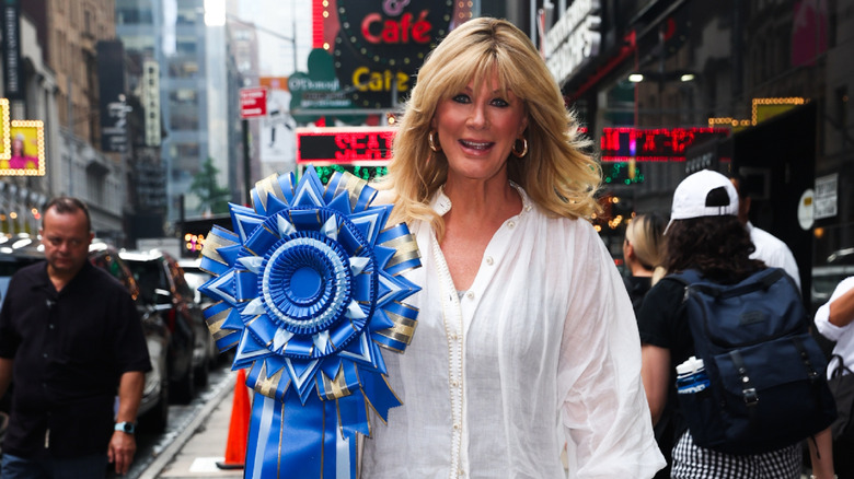 Sandra Lee walks down a city street holding a giant blue ribbon.