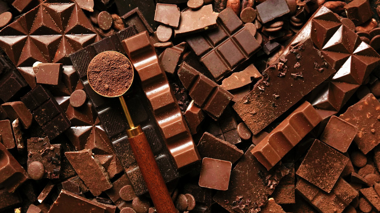 Various broken chocolates splayed on a surface and a measuring spoon of cocoa powder