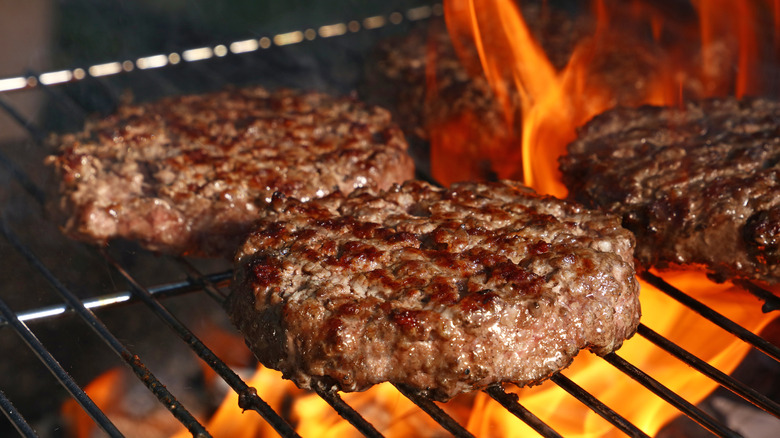 burgers cooking over a flaming grill