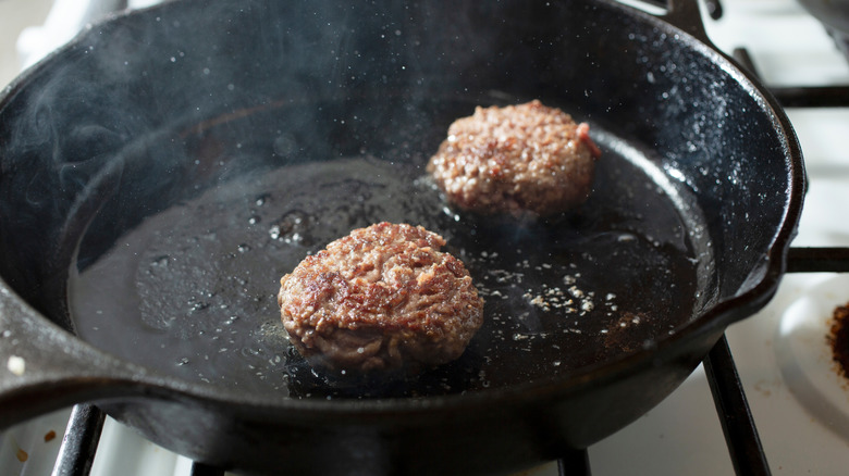 two small burgers cooking in a smoking cast iron skillet