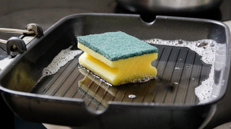 Yellow kitchen sponge in a grill pan with soapy water