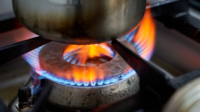 Apart on a gas stove top with blue and orange Flames burning under it
