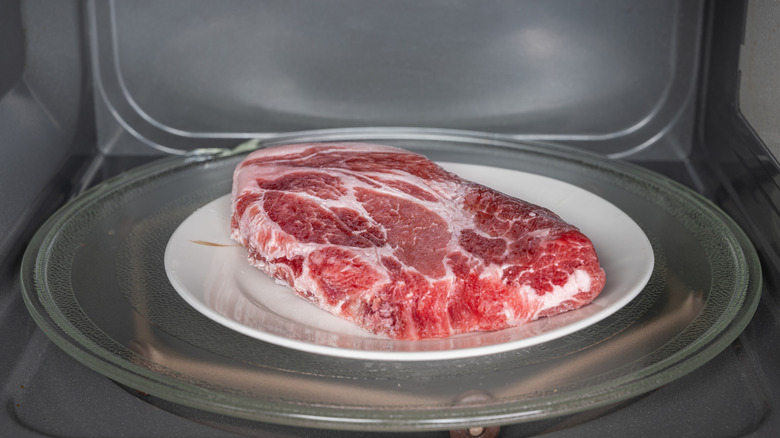 A raw steak sits on a plate in a microwave