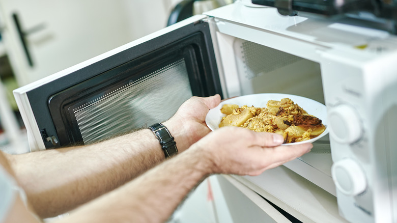 A person takes a plate of food from the microwave