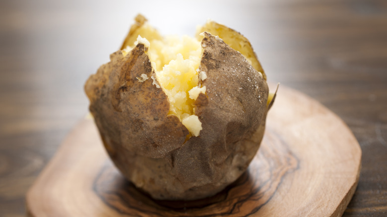 scored baked potato opened and fluffed on a wood surface