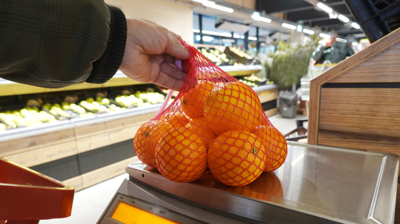 hands holding a bag of oranges on a scale in a grocery store produce department