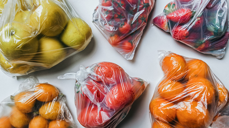 several plastic bags filled with various fruits and vegetables on a grey surface
