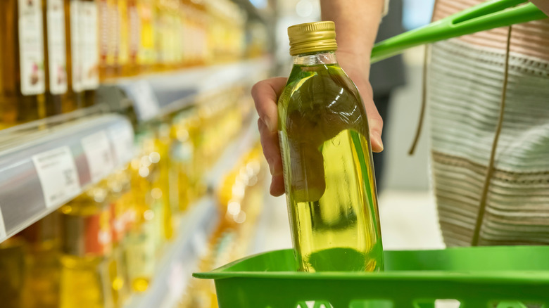 Person placing a bottle of olive oil in a basket at the grocery store