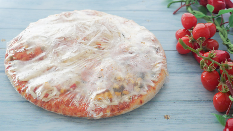 A wrapped frozen pizza next to small tomatoes on a vine