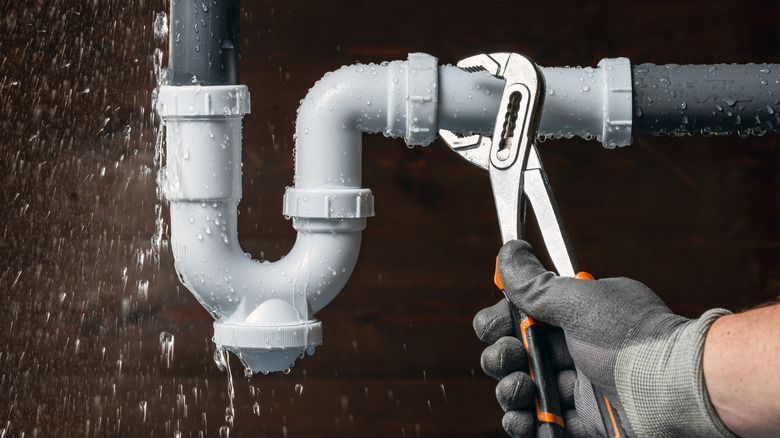 Leaking pipes under a kitchen sink with someone is trying to fix with pliers