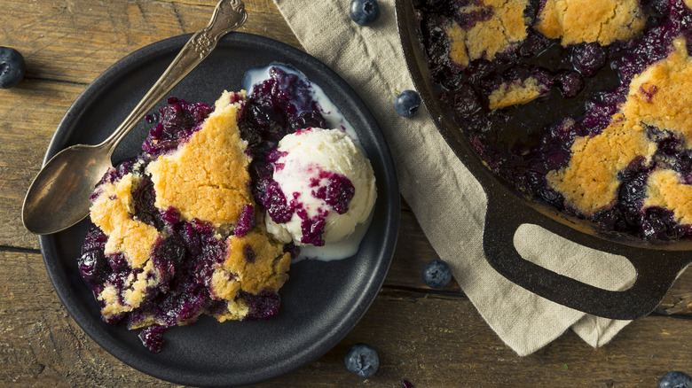 Blueberry cobbler on a black plate served with ice cream