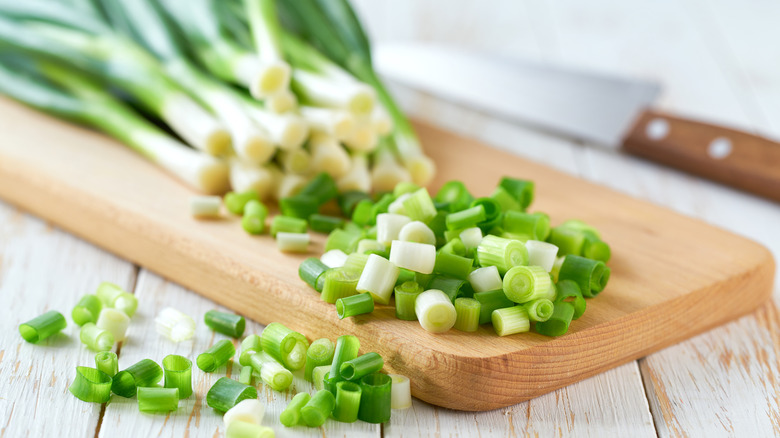 A pile of partially chopped green onions on a wooden cutting board