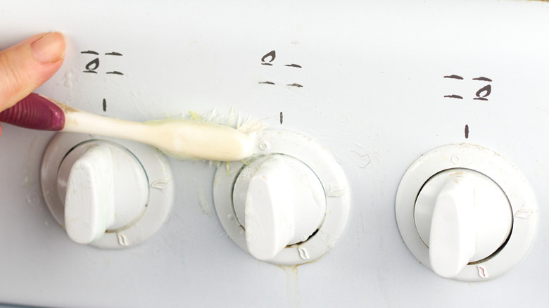 Someone uses a toothbrish to clean around the dial of a stove