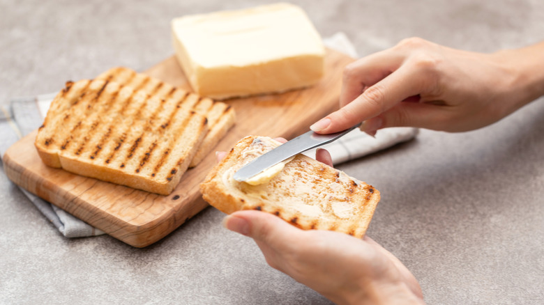 hands butter grilled bread with knife next to wooden board