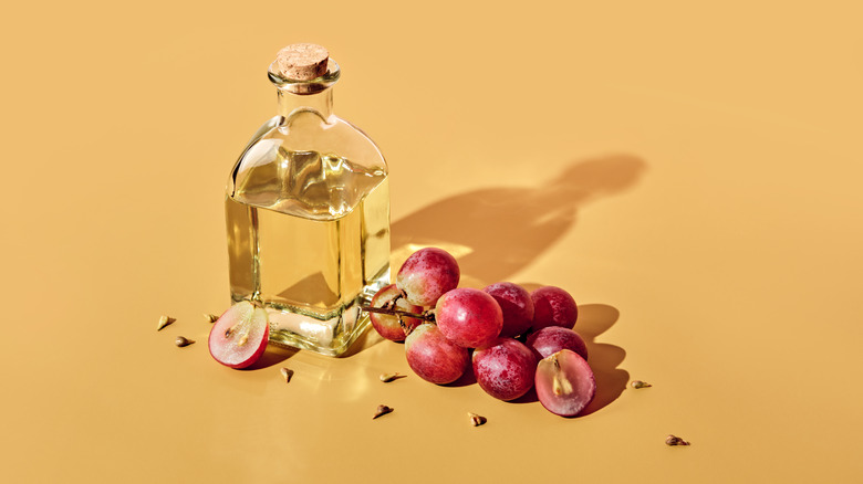 bottle of grapeseed oil staged with grapes and grapeseeds on yellow backdrop