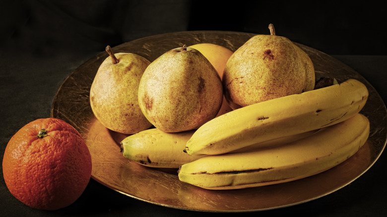 Pears, bananas, and an orange in a bowl together