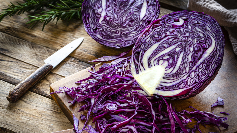 Red cabbage head sliced in half with shredded cabbage and a knife next to it