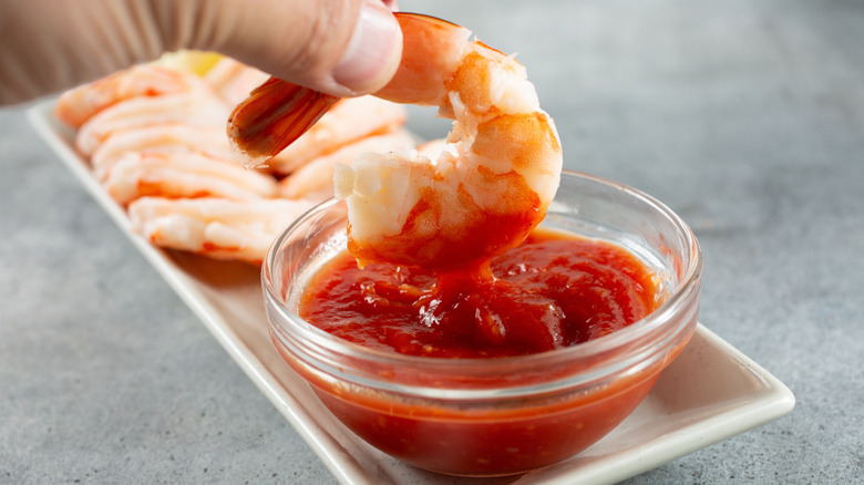 hand dipping a shrimp into small glass bowl of cocktail sauce