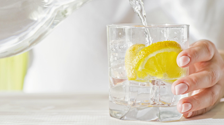 Person pouring water into a glass with lemon slices