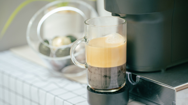 A brewed espresso in a glass under a Nespresso machine